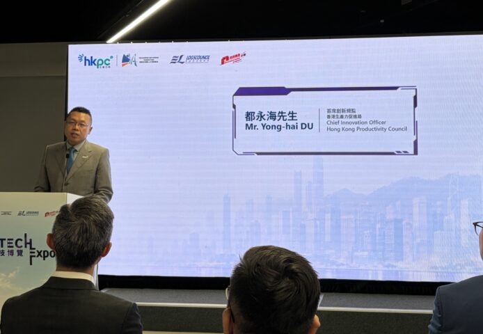 機械狗在展台前巡檢，背後大屏幕顯示人名與職位.