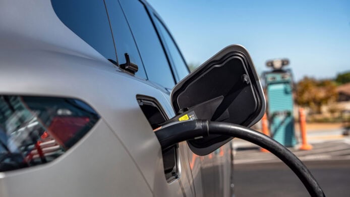 BMW 探路電動車充電場景 車輛插頭充電口特寫,背景為自動充電樁與街區.